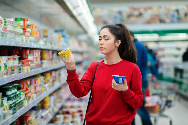 una giovane bella donna caucasica sceglie tra due yogurt. il concetto di consumismo e shopping - supermarket shopping retail choice foto e immagini stock