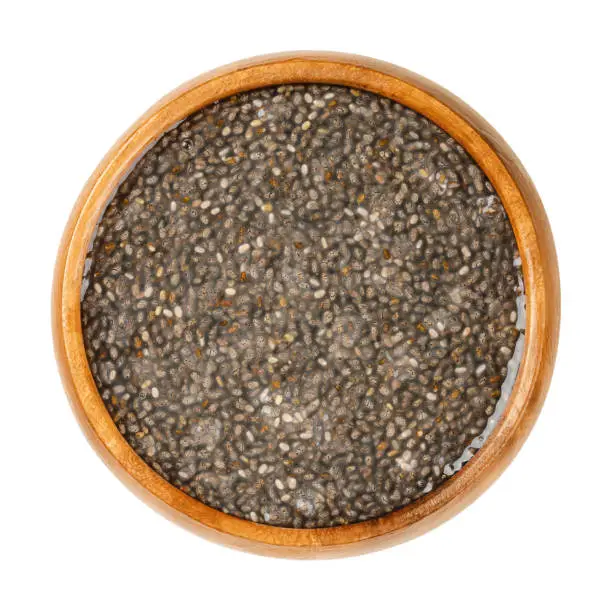 Raw chia seeds, soaked in water, in a wooden bowl. Fruits of Salvia hispanica, very hygroscopic, absorbing twelve times their weight, giving food a gel texture. Close-up, from above, macro food photo.