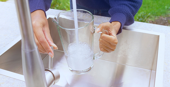 Close-up of woman's hand filling pitcher with water in garden sink.