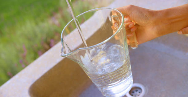 Close-up of woman's hand filling pitcher with water in garden sink.