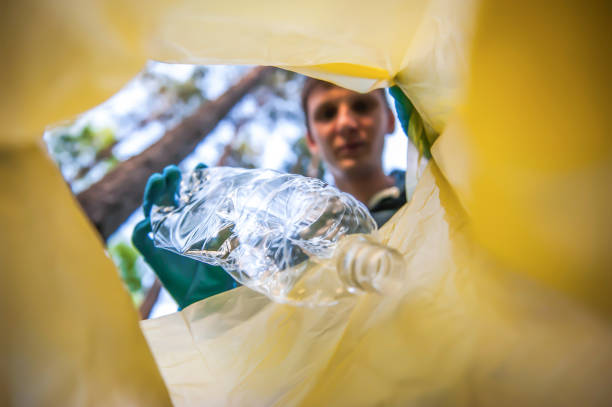 istock Garbage collection in nature. Young man puts plastic trash in a yellow bag, inside view 1318811070