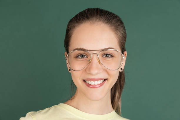 Smiling, smart. Caucasian young woman's portrait isolated on green studio background with copyspace for ad. Beautiful model with glasses. Concept of human emotions, facial expression, youth culture.