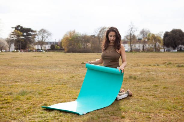 одна молодая женщина свертывая вверх коврик йоги, в парке - свертывая стоковые фото и изображения