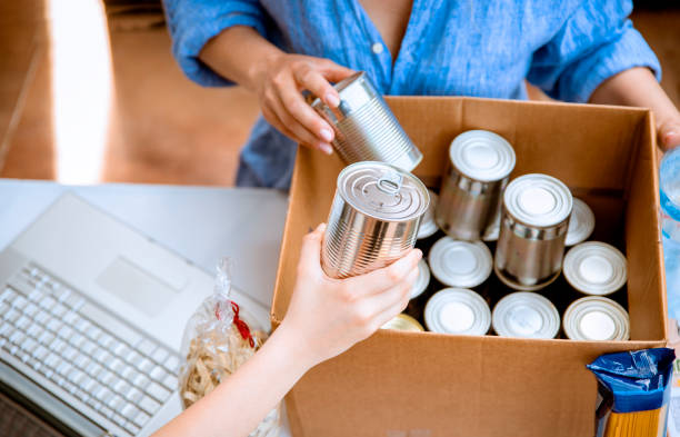Cardboard Box packing with canned food donations Volunteers collecting food into donation box. Boxing Cans at Food Drive.  Work together at food bank altruism photos stock pictures, royalty-free photos & images