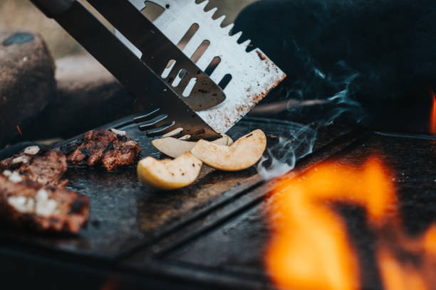 istock Wonderfully fragrant and crispy pork neck is prepared on a granite stone on an open fire. Next, a man prepares a baked apple as a dessert for the main course. Outdoor seating. Tenting, camping 1318827861
