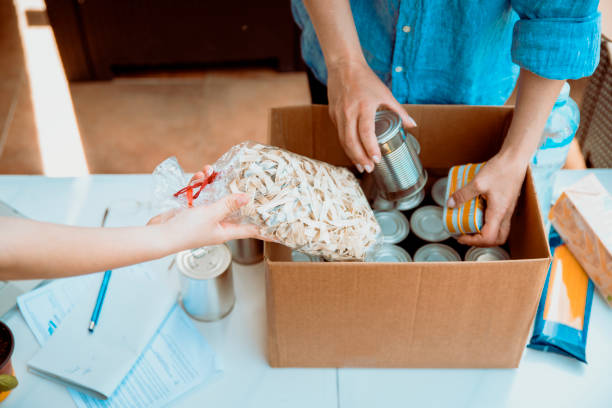 Working at food bank Volunteers collecting food into donation box. Cut out middle section image of hands packing Cans at Food Drive food bank stock pictures, royalty-free photos & images