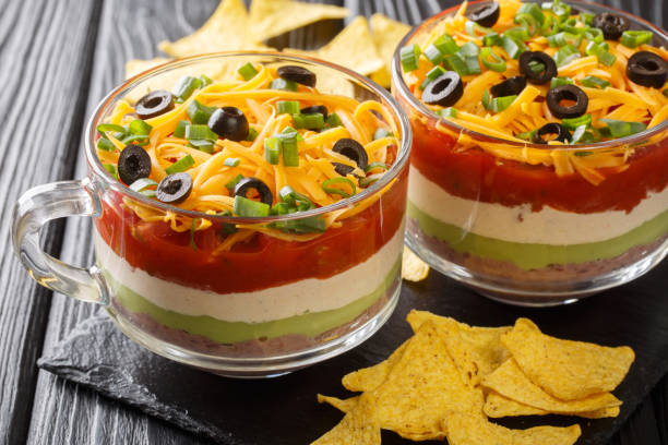 Classic Mexican 7 Layer Dip with corn chips close up in the glass. Horizontal Classic Mexican 7 Layer Dip with corn chips close up in the glass on the table. Horizontal onion layer stock pictures, royalty-free photos & images