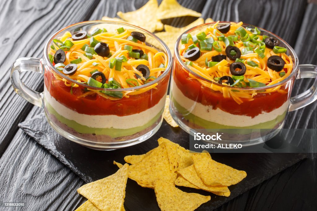 Delicious food appetizer Mexican seven-layer dip salad served with chips close-up. horizontal Delicious food appetizer Mexican seven-layer dip salad served with chips close-up on the table. horizontal Dipping Sauce Stock Photo