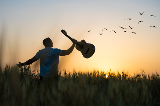 Musician holding acoustic guitar in hand of silhouette on sunset background