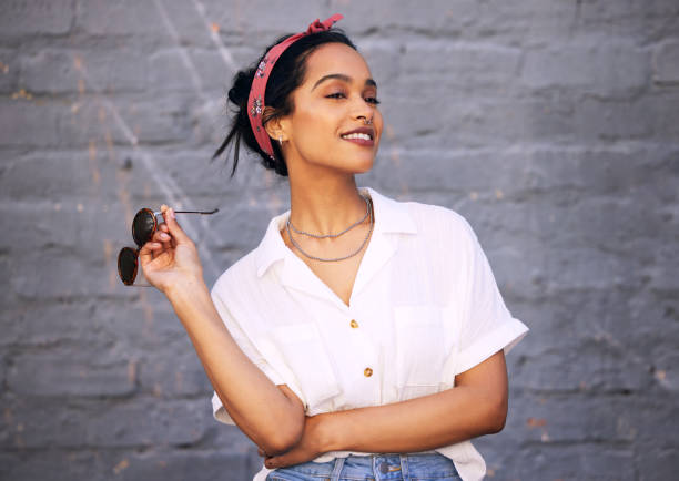 foto de una atractiva joven de pie sola contra una pared gris afuera y posando durante el día - women fashion summer fashion model fotografías e imágenes de stock