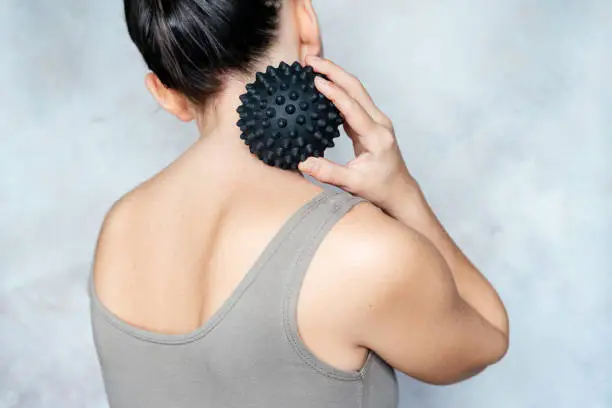 Young woman massages her back with spiky trigger point ball, muscle pain treatment reflexology, deep tissue massage