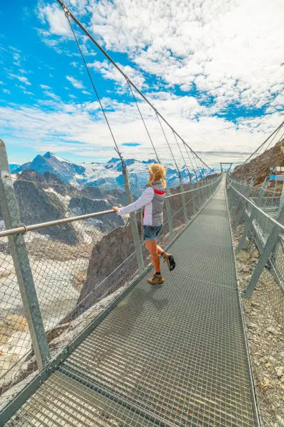 Woman with Swiss flag on Titlis cliff walk suspension bridge. Top of Titlis mountain with glacier in the Uri Alps in season. Viewpoint 3028 m in canton of Obwalden, Switzerland, Europe. vertical view