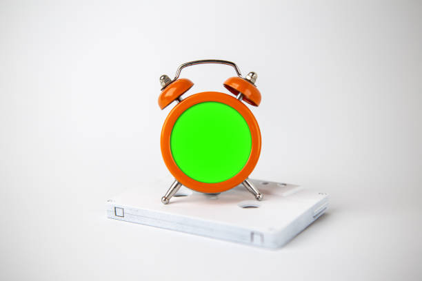 an orange analog alarm clock is located on a white audio cassette. the clock has a green background to add content. minimal concept of music and time. - clock time alarm clock orange imagens e fotografias de stock