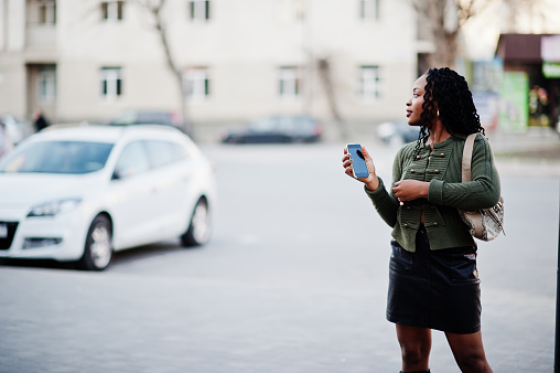 Stylish fashionable african american women in green sweater and black skirt posed outdoor with mobile phone.