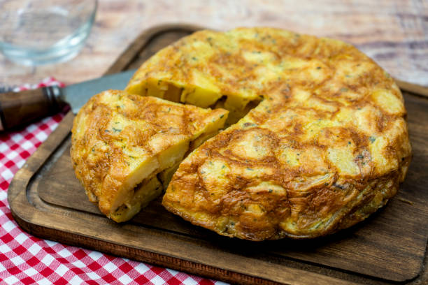 tipica frittata spagnola di patate o tortilla de papas con una porzione tagliata in un ambiente rustico. cucina spagnola. visualizzazione normale. - tortilla de patatas foto e immagini stock