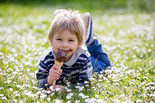 Cute blond child, boy, eating ice cream in the park, springtime