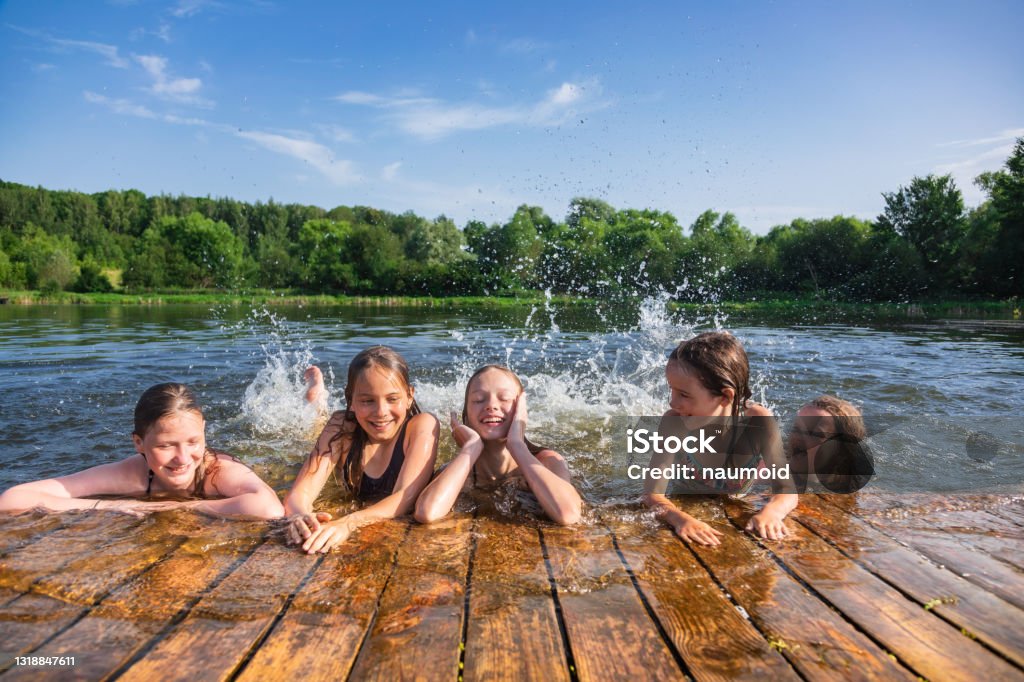 Happy children enjoying summer holidays at a lake Happy little girls having fun playing in a lake splashing water during summer holidays Lake Stock Photo