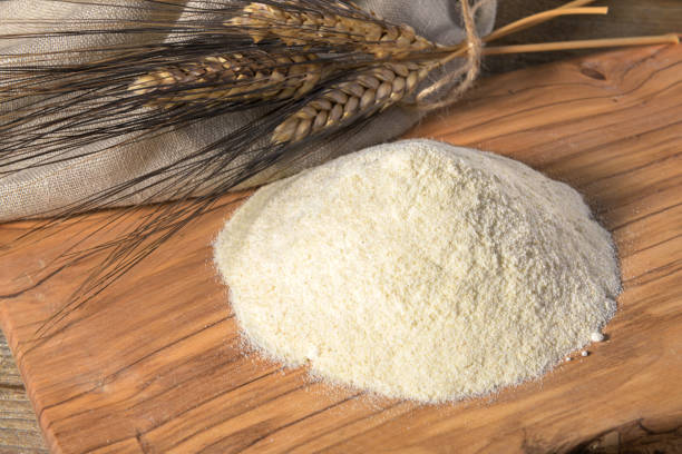 Wheat flour on a wooden cutboard and spikelets on a wooden table, close up