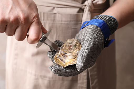 Man opening fresh oyster with knife, closeup