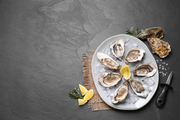 istock Delicious fresh oysters with lemon slices served on black slate table, flat lay. Space for text 1318850366