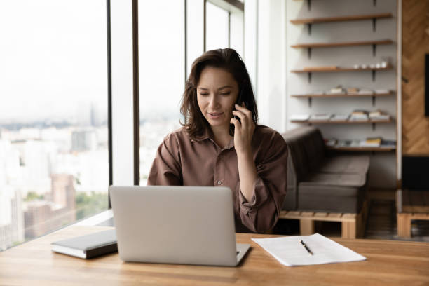istock Young female employee work on laptop talk on cell 1318858264