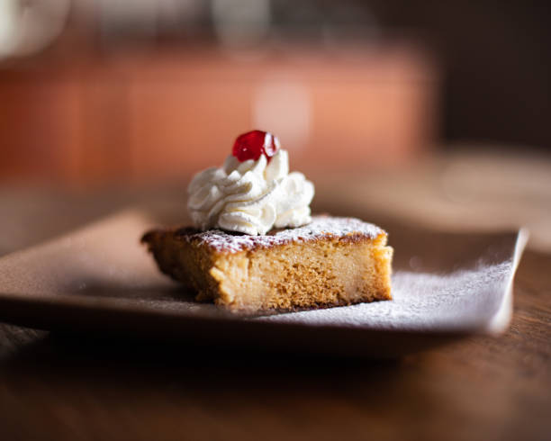Dessert with cream and red cherry on brown plate Bokeh photo of malva pudding with cream and red cherry on brown plate malva stock pictures, royalty-free photos & images