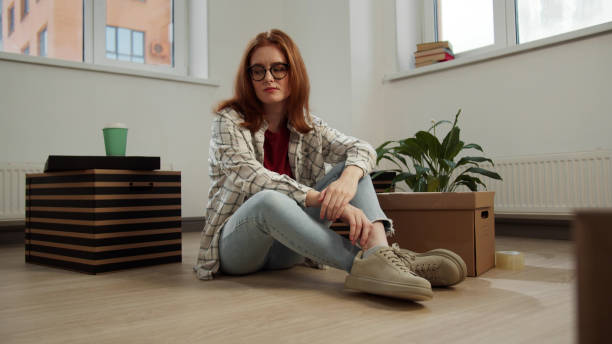 eine frau sitzt auf dem boden und betrachtet ihre dinge mit unmut - solitude loneliness hardwood floor box stock-fotos und bilder