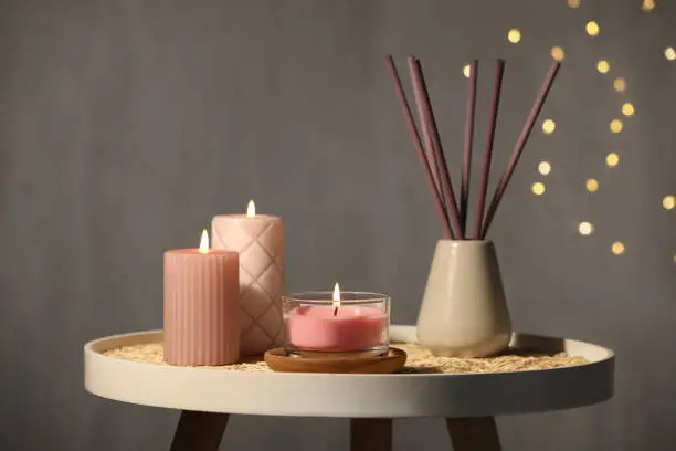 Burning candles and reed diffuser on table against grey background