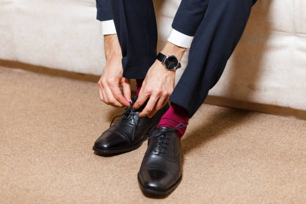 A businessman in dark blue suit, red socks and watches tying his shoelaces of black shoes. Modern, stylish and expensive look for young man A businessman in dark blue suit, red socks and watch tying his shoelaces of black shoes. Modern, stylish and expensive look for young man dinner jacket stock pictures, royalty-free photos & images
