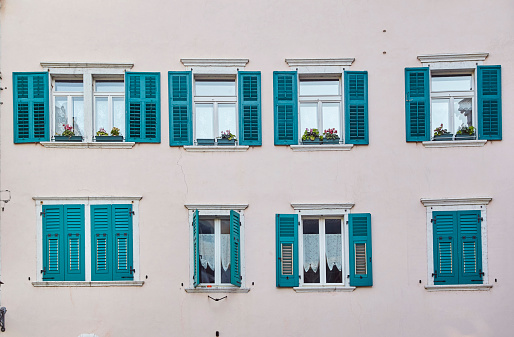 Eight classic italian windows on the bright pink wall facade with wooden ultramarine color shutters