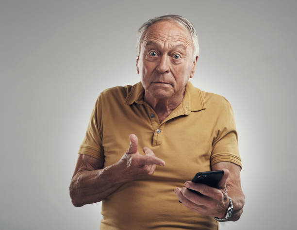 Studio shot of an elderly man using his cellphone against a grey background You know how to operate this thing? wtf stock pictures, royalty-free photos & images
