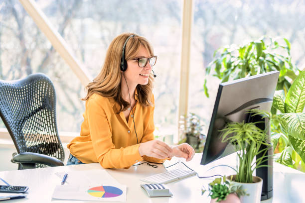 Shot of call center agent operator businesswoman working from home Mature businesswoman in headset speaking by conference call while looking at computer. Home office. hands free device stock pictures, royalty-free photos & images