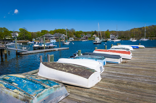 A row of small rowboats on a dock on Eel Pond in Woods Hole, Massachusetts await their owners to take them to their moored yachts offshore.