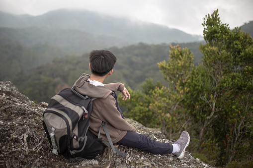 Asian Chinese teenager boy sitting on rock looking at view in Cameron Highland