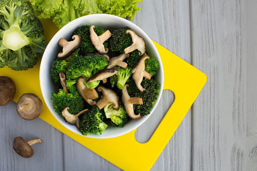 Vegetarian salad with mushrooms shiitake and broccoli in the white bowl on the gray wooden  background. Top view. Copy space.
