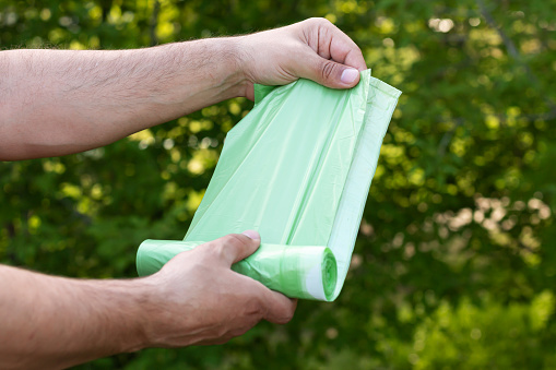 Man holding eco plastic garbage bio bag in roll outdoors, bag for composting organic trash