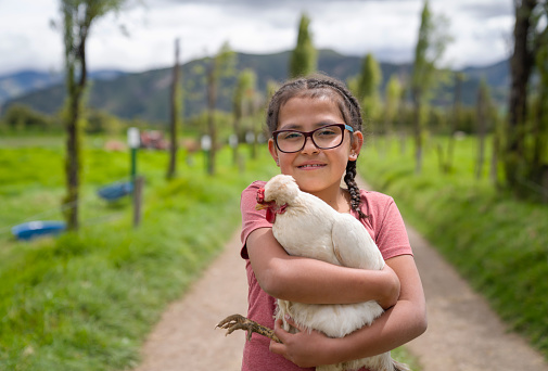 Portrait of a happy Latin American girl holding a chicken at a farm and looking at the camera smiling - poultry concepts