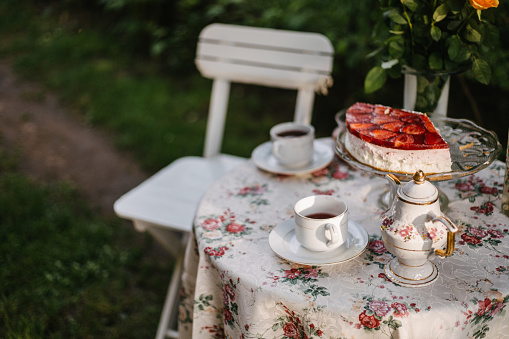 Garden table with teacups, teapot and strawberry cake on