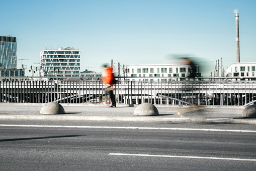 view on motion blurred pedestrian and cyclist on bridge in modern city district in Berlin under blue sky