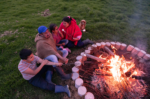 Happy Latin American family having a bonfire and having fun eating marshmallows- lifestyle concepts