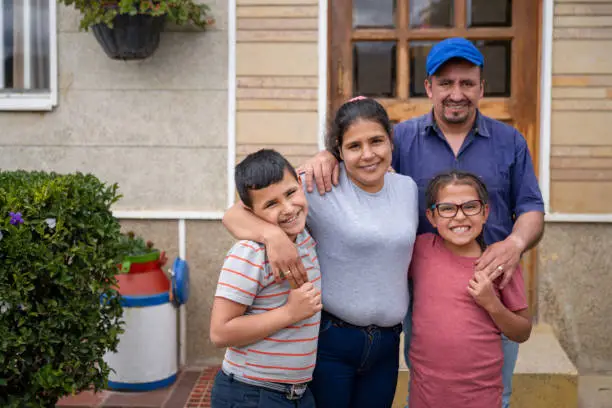 Portrait of a rural Latin American family in front of their new house and looking at the camera smiling - housing policy concepts