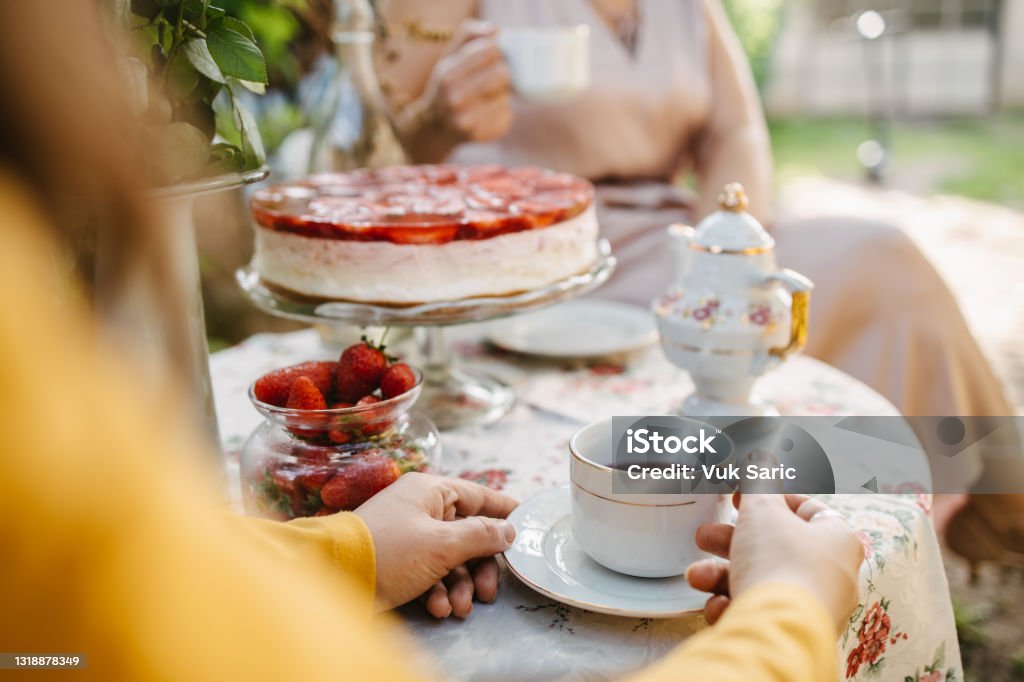 Woman holding a teacup on the garden table A young adult woman holding a teacup on the garden table during a tea party in the garden. Afternoon Tea Stock Photo