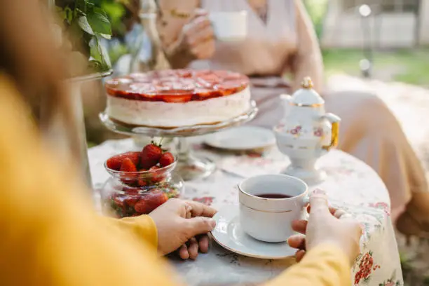 A young adult woman holding a teacup on the garden table during a tea party in the garden.