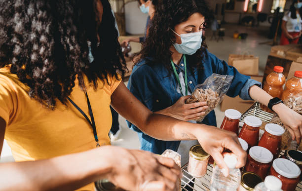 Two women are arranging food and drinks on the shelves - Close up shot Two women are arranging food and drinks on the shelves - Close up shot. They are preparing a food and clothes bank. food bank stock pictures, royalty-free photos & images