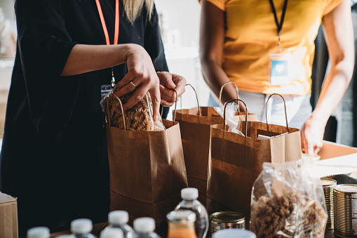 Close up photo of volunteers preparing donation bags with food at the food and clothes bank. Jars, cans, food and drink on the table.