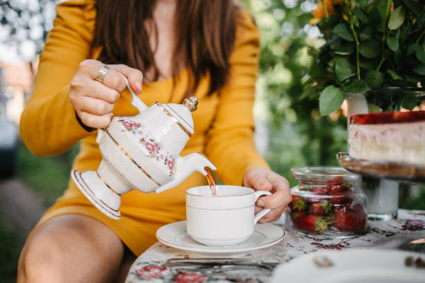 kobieta wylewająca herbatę z czajnika do filiżanki do herbaty - afternoon tea tea women table zdjęcia i obrazy z banku zdjęć