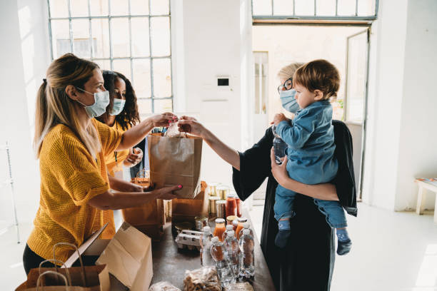 A mother with her little son is taking a bag of food at the food and clothes bank A mother with her little son is taking a bag of food at the food and clothes bank. People are wearing protective face masks. food bank stock pictures, royalty-free photos & images