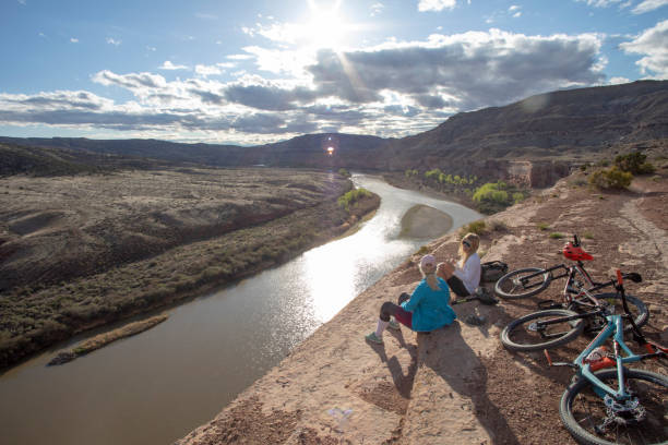 Mother and daughter mountain bikers relax on canyon ridge above river Mother uses mobile phone fruita colorado stock pictures, royalty-free photos & images