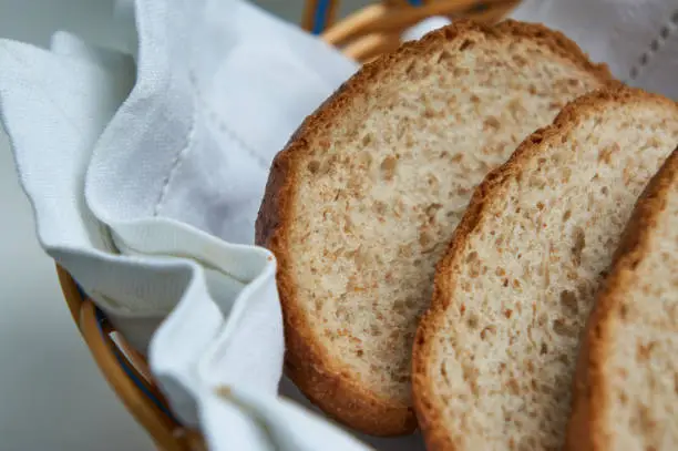 Cut grain bread in breadbasket with white towel close up