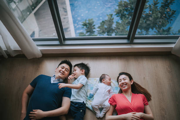 direkt über asiatischen chinesischen jungen familie auf holzböden im wohnzimmer lächelnd liegend - women group of people lying down mother stock-fotos und bilder